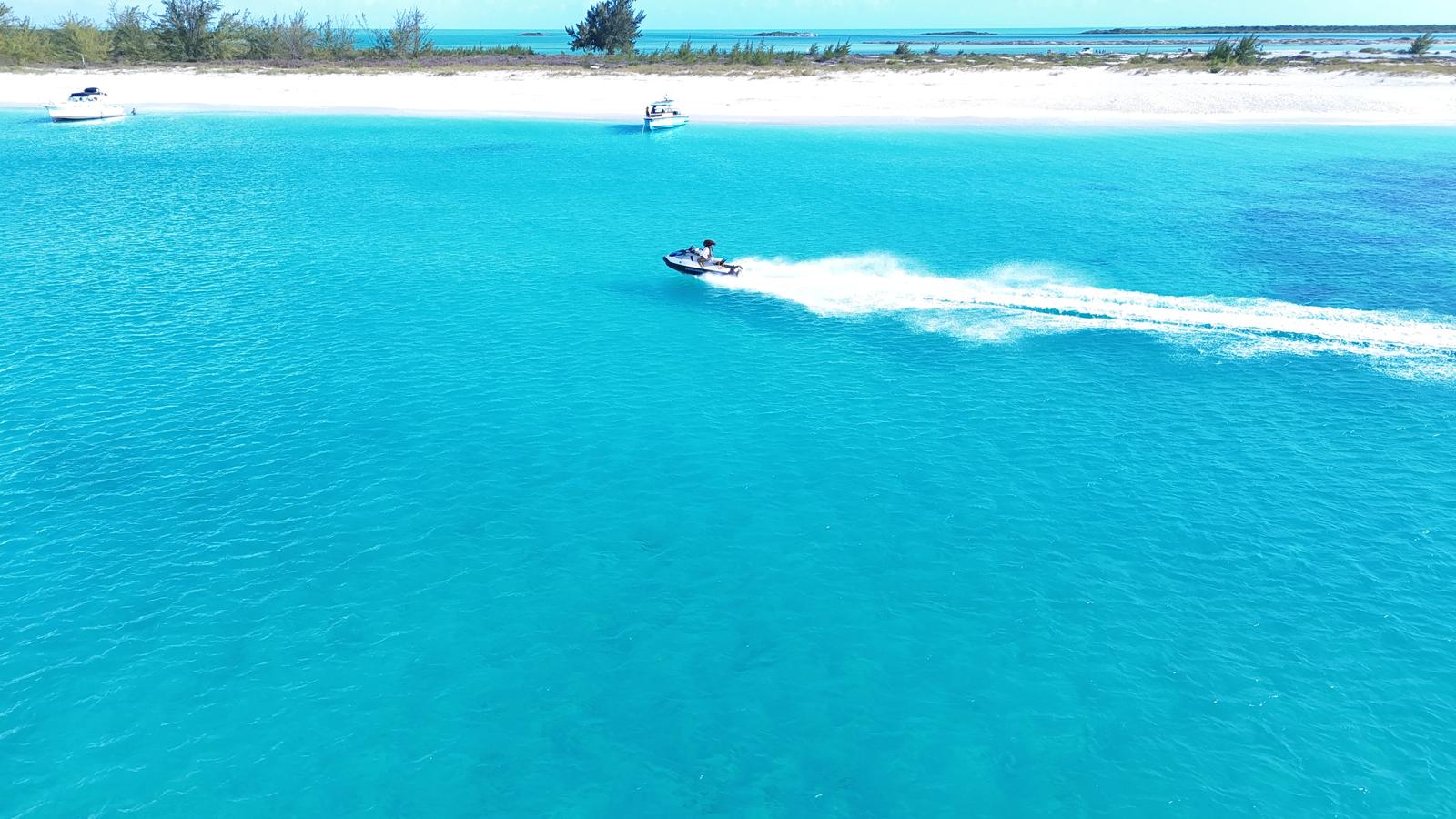 Aerial view of a jet ski carving through turquoise water beside a white sandbar